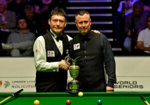 Jimmy White and Alfie Burden shake hands in front of the World Seniors Snooker Championship trophy before their 2023 final.